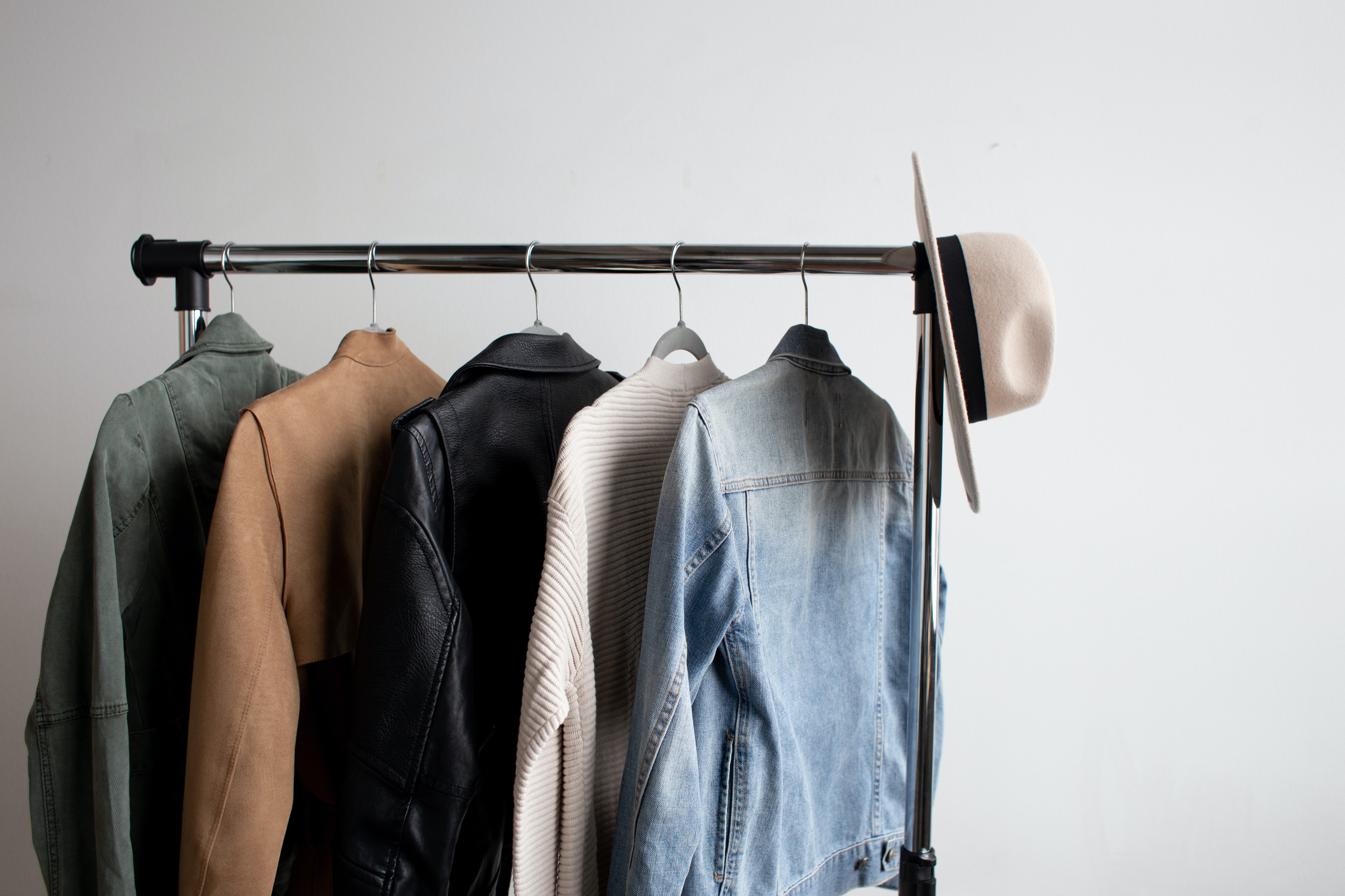 a metal clothes rail against a white wall with various clothes hanging and a hat balanced on the end